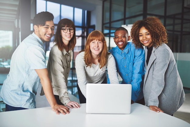 Moderne technologie geeft de voorsprong op bijgesneden portret van een groep jonge zakenmensen die ineengedoken rond een laptop in hun kantoor zitten