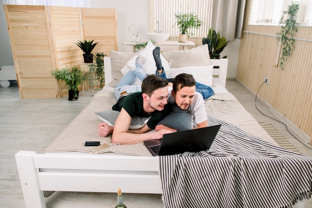 Moderne technologie. Vrij jong homopaar die laptop met behulp van terwijl het stellen op bed en samen tijd doorbrengen