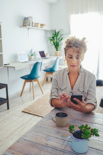 Moderne volwassen vrouw die thuis mobiele telefoon gebruikt om berichten te verzenden en op internet te surfen. gelukkige vrouwelijke volwassen mensen genieten van een technologische verbinding in de woonkamer met een mobiel apparaat