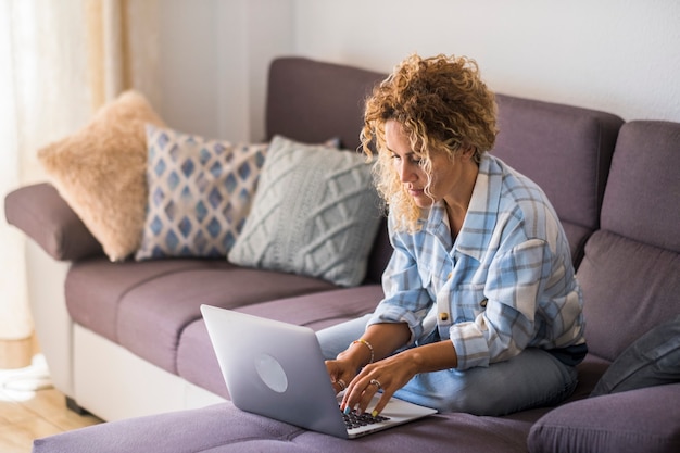 Moderne vrouw die op de bank ligt en laptopcomputer gebruikt voor werk of surfen op het web - volwassen vrouwelijke mensen genieten van internettechnologie in slim werken en beheer van de thuiseconomie - portret van dame