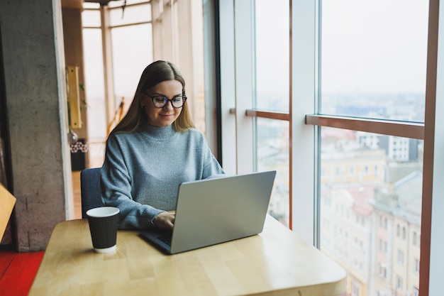 Moderne vrouwelijke kantoormedewerker in vrijetijdskleding werkt op een laptop Vrouwelijke manager op de werkplek werkt aan een nieuw project met behulp van de moderne werkruimte van de laptop