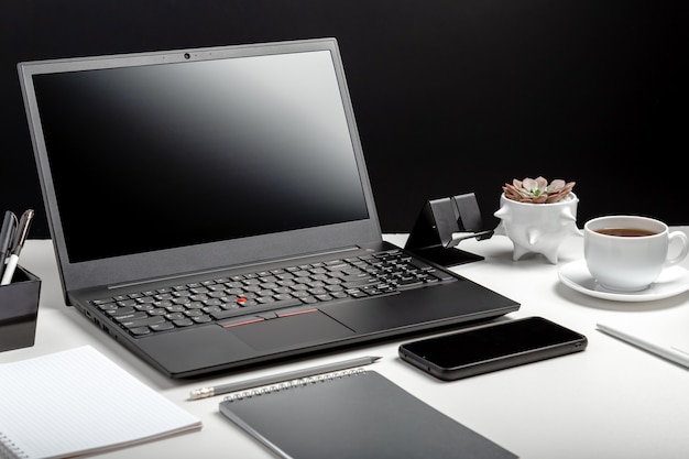Moderne werkplek. Thuiskantoor laptop scherm leeg scherm werkruimte. Desktop met laptop pc smartphone, kantoorleveranciers, koffiekopje plant bloem. Bureau tafel zwarte achtergrond.