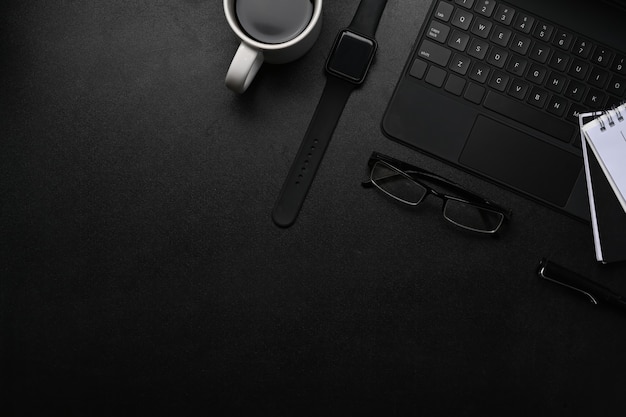 Moderne werkruimte met slim horloge, notebook, toetsenbord en bril op zwarte tafel.