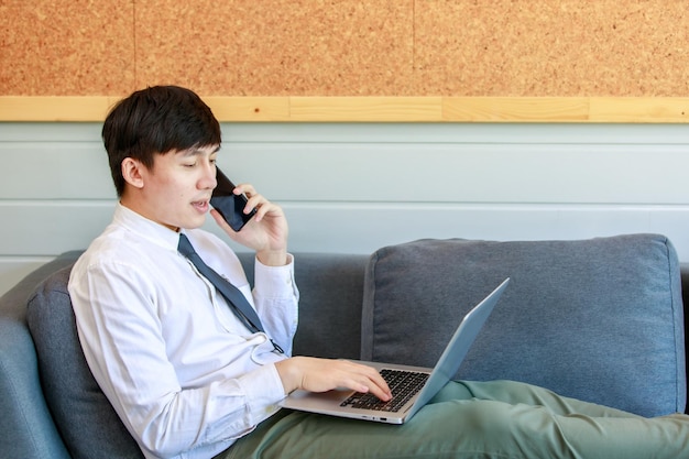 Moderne zakenlieden gaan op de bank in de lobby liggen voor ongedwongen ontspanning door de benen te strekken en te werken met comfortabele laptops voor online communicatie en het vasthouden van een smartphone