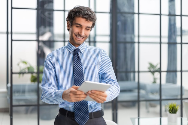 Moderne zakenman die digitale tablet gebruikt terwijl hij op kantoor staat