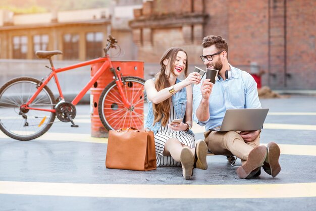 Moderne zakenman en zakenvrouw werken met laptop en koffie buiten op de speelplaats met fiets op de achtergrond. Lifestyle bedrijfsconcept