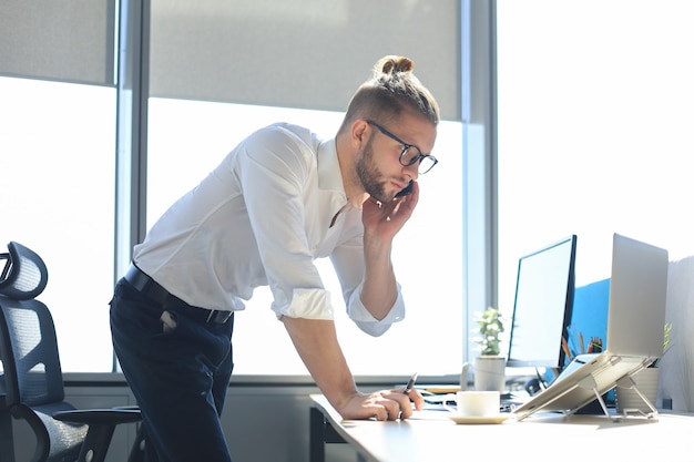 Moderne zakenman praten op de slimme telefoon en glimlachen terwijl hij op kantoor zit.