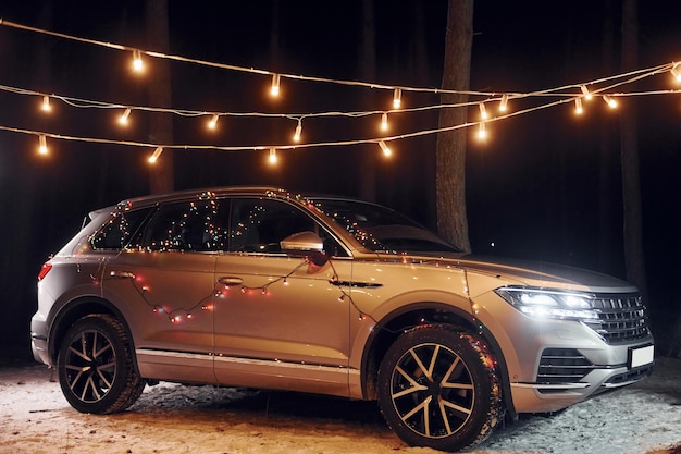 Moderne zilverkleurige auto geparkeerd in het bos met vakantiedecoratie