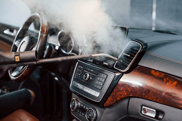 Moderne zwarte auto's worden van binnen schoongemaakt door stoomapparatuur door een werknemer in een wasstation.