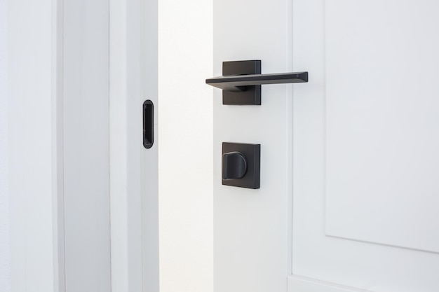 Moderne zwarte deurklink op witte houten deur in interieur Knop close-up elementen Deurkruk beslag voor interieur