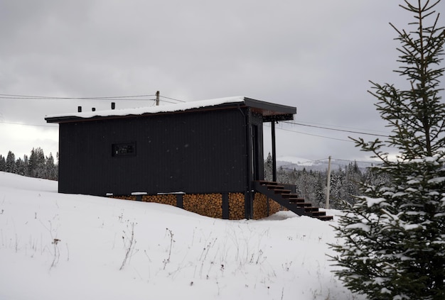 Moderne zwarte houten hut in dennenbos bij sneeuwweer