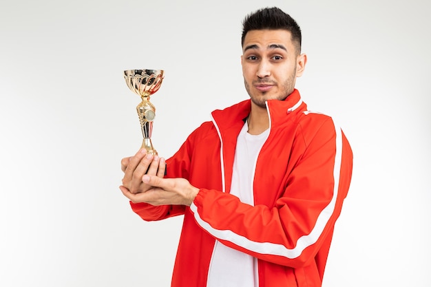 Modest athlete in a tracksuit with a golden winner cup on a white studio background.