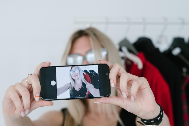 Modestylist die selfie op mobiele telefoon neemt met modieuze kleding in de levensstijl van de sociale media-influencer op de achtergrond