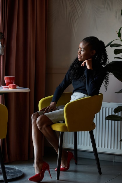 Modieus Afrikaans meisje zit aan cafétafel en geniet van ochtendcappuccino Jonge zwarte vrouw drink