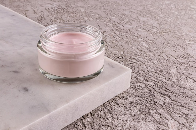 Modieus cosmetisch product in glazen pot delicate roze crème voor jonge huidverzorging op marmeren podium en grijze cement achtergrond