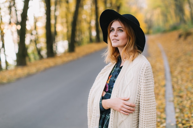 Modieus hippiemeisje in een gebreide sweater en hoedengangen in het de herfstpark.