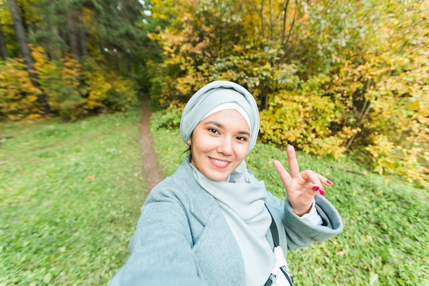 Modieus jong moslim Aziatisch meisje in hijab die een selfie neemt op smartphone buiten in het herfstpark