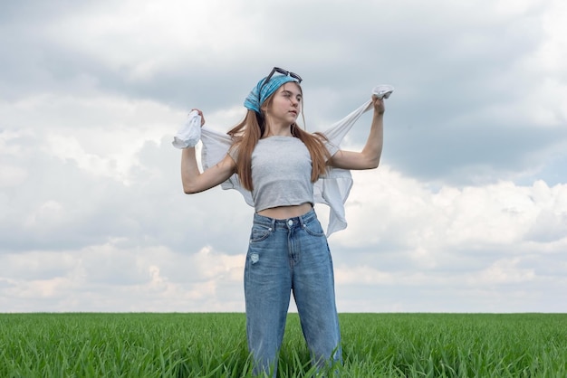 Modieus klein tienermeisje in een veld van groen gras tegen een achtergrond van bewolkte hemel