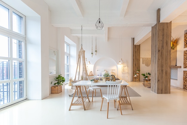 Modieus modern interieur van een licht studio-appartement met houten kolommen in de loft-stijl, versierd met baksteen, marmer en hout met stijlvol meubilair en witte muren