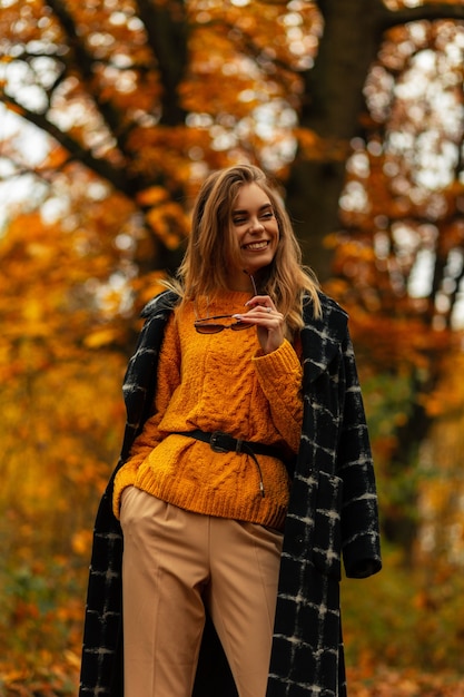 Modieus mooi lachend meisje in stijlvolle herfstkleren loopt in een gouden herfstpark met geel gebladerte