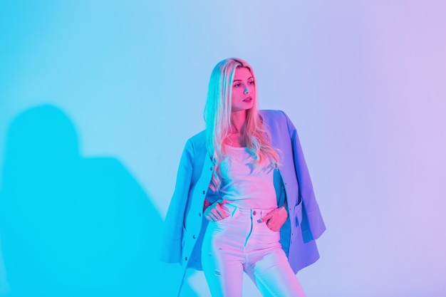 Modieus vrij glamoureus meisje in een stijlvol pak met een blauwe blazer op pastelkleuren neonroze lichten in studio