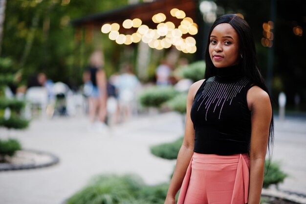 Modieuze Afro-Amerikaanse vrouw in perzik broek en zwarte blouse poseren buiten.