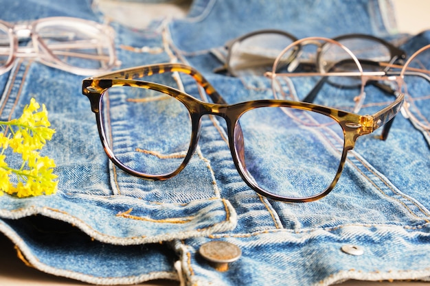 Modieuze bril op een spijkerjasje, een oud jasje van spijkerbroek en meerdere brillenglazen, trendy brilmonturen