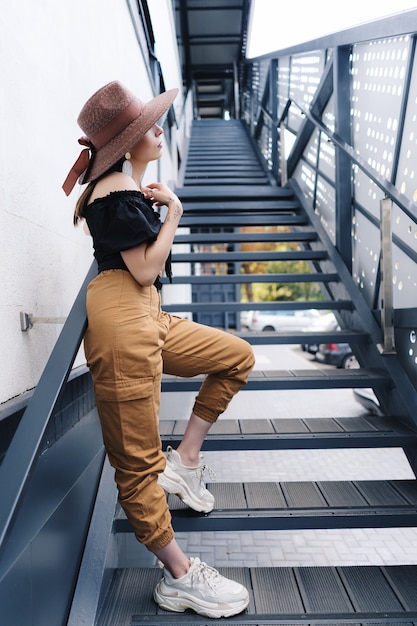 Modieuze brunette vrouw met lang haar, stijlvolle grote rieten hoed dragen, die zich voordeed op de trap.