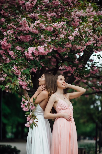 Modieuze dame poseert in de buurt van een bloeiende boom. Twin Girls Schoonheid en mode voor dames.