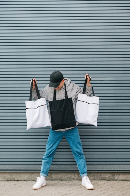Modieuze foto van een jonge man in streetwear met eco tassen in zijn handen.