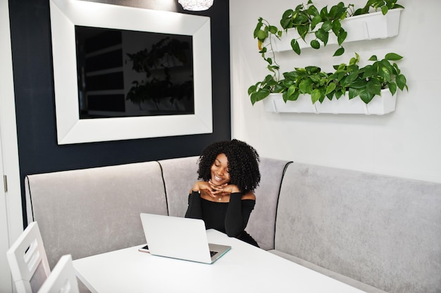 Modieuze jonge mooie Afro-Amerikaanse zakenvrouw met afro kapsel slijtage in elegante zwarte zitten en werken op laptop