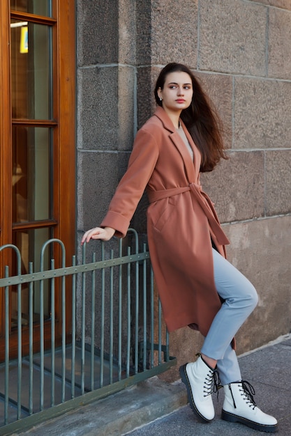 Modieuze jonge mooie stijlvolle vrouw in bruine jas lopen op straat. Herfstmodetrend voor lachende, vrolijke, doelgerichte vrouwen. Conceptstijl, mode, schoonheid en prestatiedoelen. Ruimte kopiëren