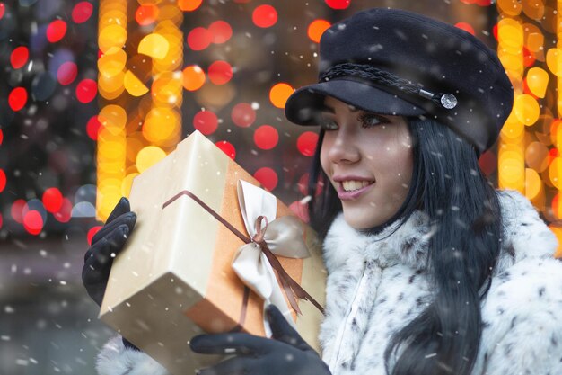 Modieuze jonge vrouw die cadeau krijgt op de vakantiebeurs tijdens sneeuwval. Lege ruimte