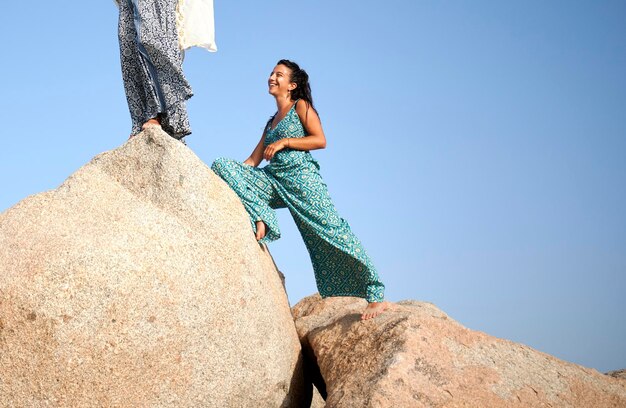 Modieuze jonge vrouw op een rots glimlachend onder een heldere blauwe hemel