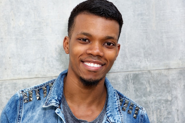 Modieuze jonge zwarte man glimlachend staande door muur