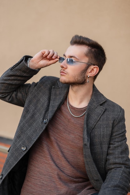 Modieuze knappe hipster man met haar in een stijlvolle jas draagt vintage zonnebril in de stad