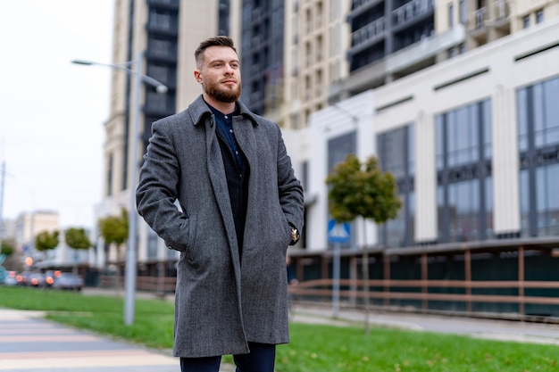 Modieuze man in jas staat in de buurt van kantoorcentrum en kijkt vooruit Zakelijke persoon blijft kalm en denken Succesvol concept Doordachte en resolute blik van knappe man in grote stad