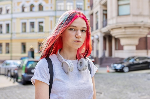 Modieuze mooi meisje tiener 16, 17 jaar oud met draadloze koptelefoon met fel geverfd gekleurd kapsel op straat van de zomer zonnige stad. Lifestyle, jeugd, mode, schoonheid