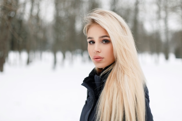 Modieuze mooie jonge vrouw in een trendy elegante jas in het park op een besneeuwde winterse dag