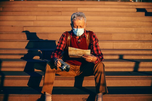 Modieuze senior man met beschermend gezichtsmasker op en zittend op de trap.