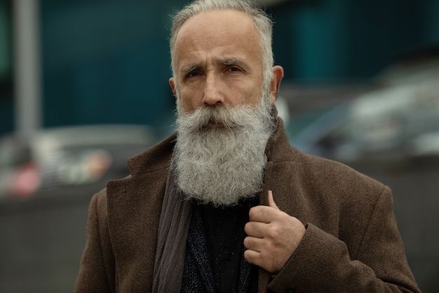 Modieuze senior man met grijs haar en baard is buiten op straat.