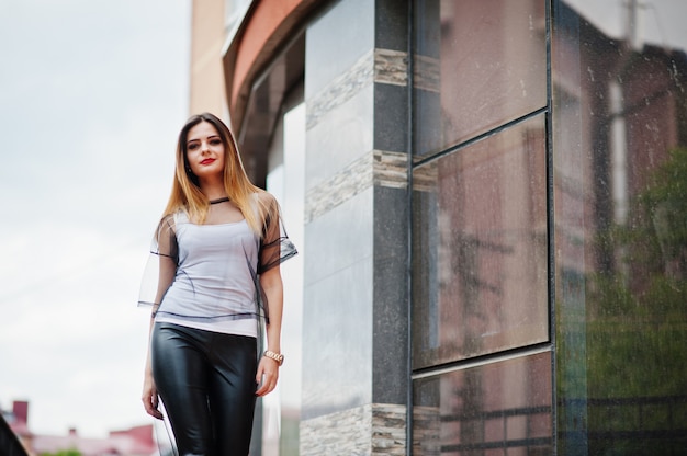 Modieuze vrouw kijkt naar wit shirt, zwarte transparante kleding, lederen broek, die zich voordeed op straat