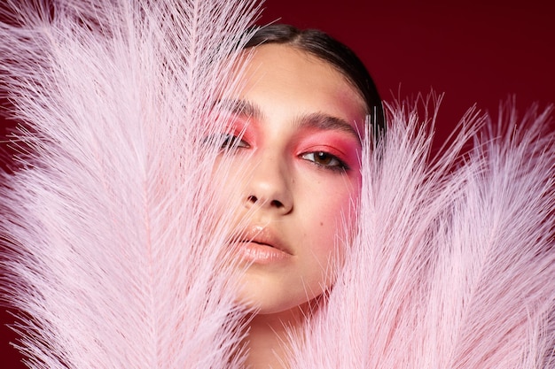 Modieuze vrouw met een kam lichte make-up poseren pluizige veren roze achtergrond ongewijzigd
