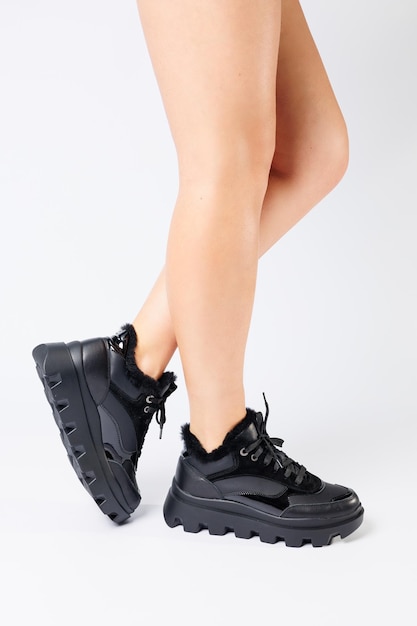 Modieuze zwarte sneakers op de benen van een vrouw in de studio op een witte achtergrond Benen van een jong meisje met mooie trendy schoenen