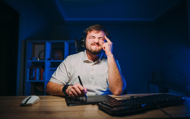 Moe bebaarde man freelancer in koptelefoon werkt 's nachts in een kamer met een blauw licht