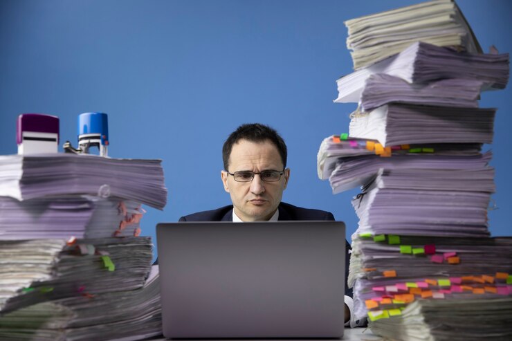 Moe bezorgd zakenman achter bureau met enorme stapel documenten