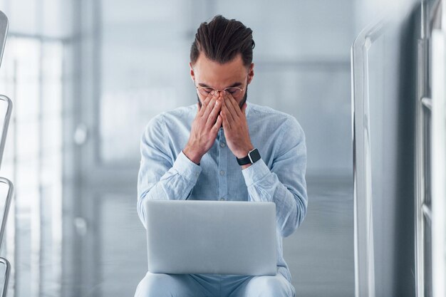 Foto moe en slecht voelen zittend op de trap met laptop jonge knappe man in formele kleding binnenshuis op kantoor overdag