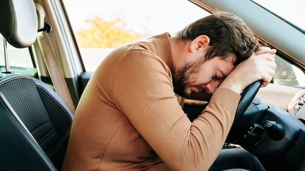Moe jonge automobilist slaapt in zijn auto met zijn hoofd op het stuur