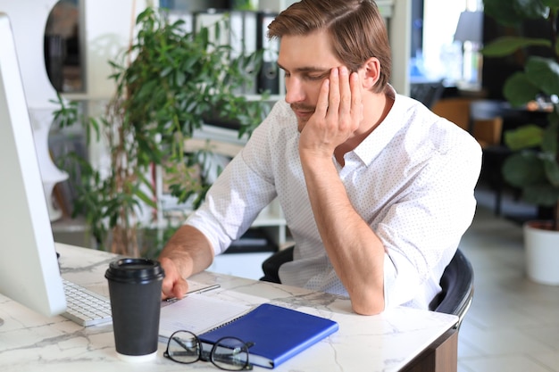 Foto moe jonge man slapen zittend met computer achter bureau op kantoor