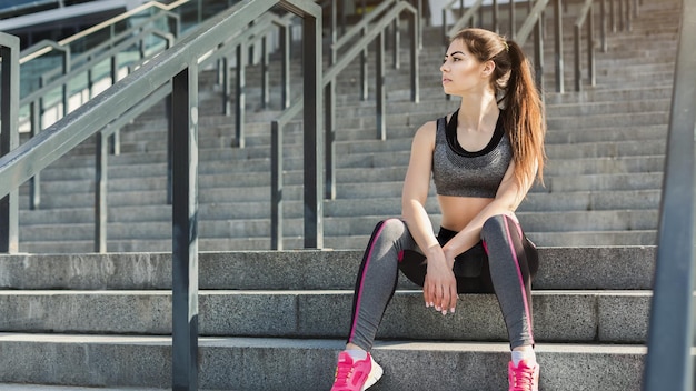 Moe jonge vrouw zittend op trappen in sportstadion